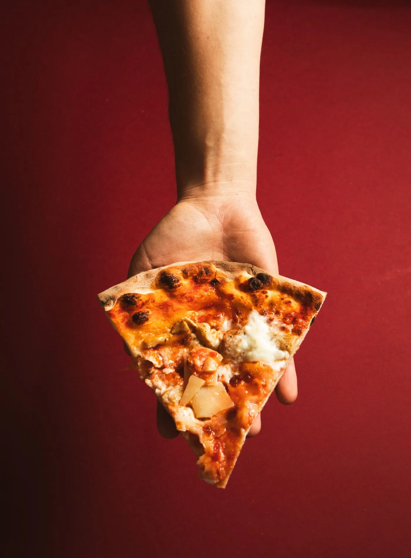Mano che regge una fetta di pizza appena sfornata della Pizzeria Jolly Blu